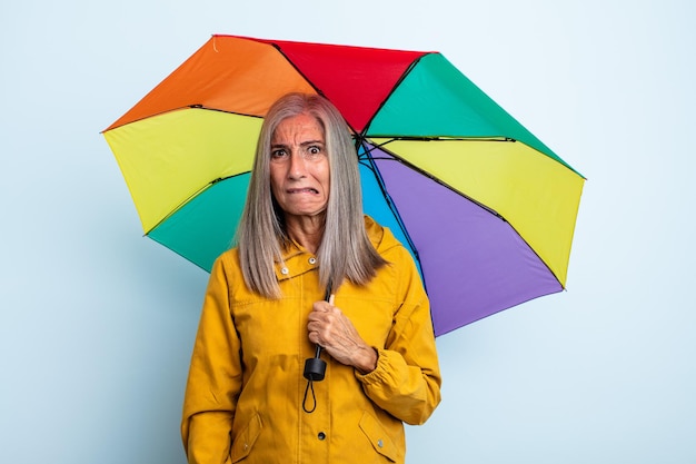 Kobieta w średnim wieku z siwymi włosami wygląda na zdziwioną i zdezorientowaną. koncepcja parasola i deszczu