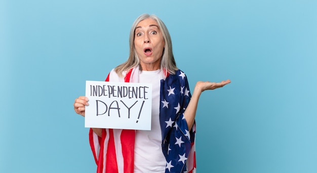 Kobieta w średnim wieku z siwymi włosami, zaskoczona i zszokowana, z opuszczoną szczęką trzymająca przedmiot. koncepcja dnia niepodległości