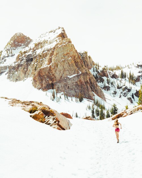 Kobieta w stroju sportowym biegnącym po zaśnieżonych polach z wysokimi górami skalistymi