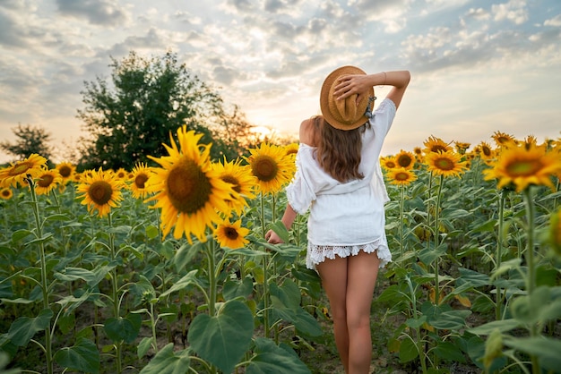 Kobieta w sukience i kapeluszu stojąca na polu ze słonecznikami