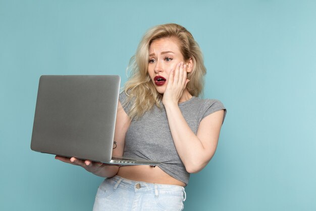kobieta w szarej koszuli i jasnych niebieskich dżinsach za pomocą laptopa