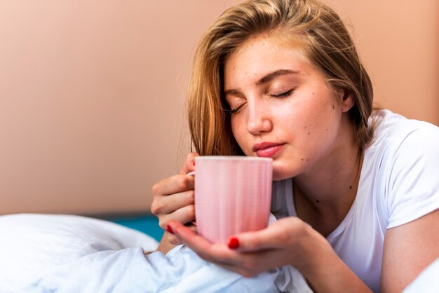 Kobieta wącha kawę podczas gdy w łóżku