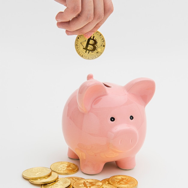 Kobieta wkładająca bitcoiny do różowej skarbonki