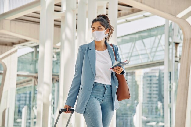 Kobieta z bagażem i maską medyczną na lotnisku podczas pandemii