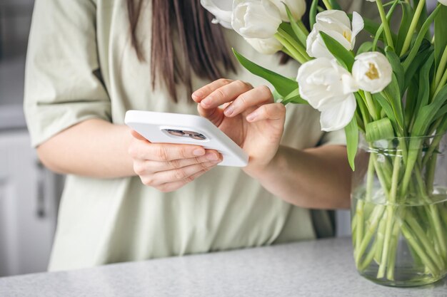 Bezpłatne zdjęcie kobieta z bukietem białych tulipanów używa zbliżenia do smartfonu