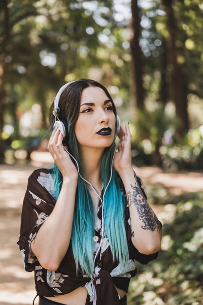 Kobieta z czarnej szminką słuchająca muzyka na hełmofonie w parku