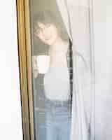Bezpłatne zdjęcie kobieta z filiżanką kawy patrząc przez okno