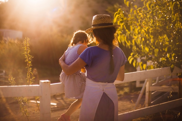Bezpłatne zdjęcie kobieta z jej córką blisko białego ogrodzenia w polu