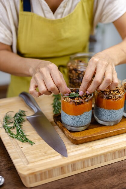 Kobieta z kolorowymi, zdrowymi, słodkimi deserami puddingami chia z mlekiem migdałowym, ekstraktem z niebieskiej spiruliny, nasionami chia, dżemem pappaya mango i domową mueslią. Na drewnianym stole w kuchni w domu.