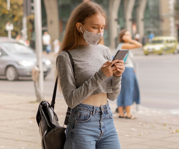 Kobieta z maską medyczną sprawdza jej telefon