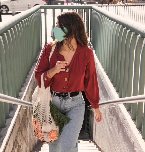 Kobieta z maską na twarz, wchodzenie po schodach na zewnątrz, trzymając torby z zakupami