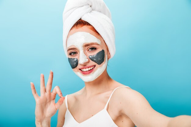 Kobieta Z Maską Pokazującą Dobry Znak I śmiejąc Się. Modelka Przy Selfie Podczas Zabiegu Spa.