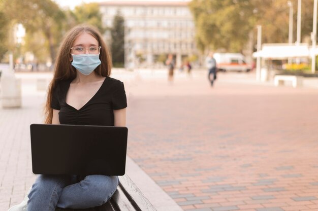 Kobieta z maską pracuje na laptopie na zewnątrz