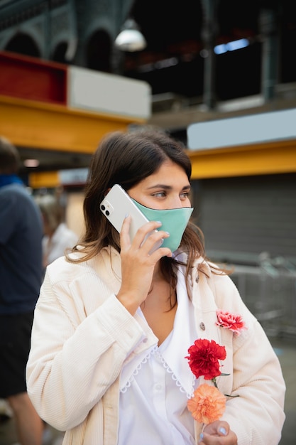 Kobieta z maską rozmawia przez telefon trzymając kwiaty