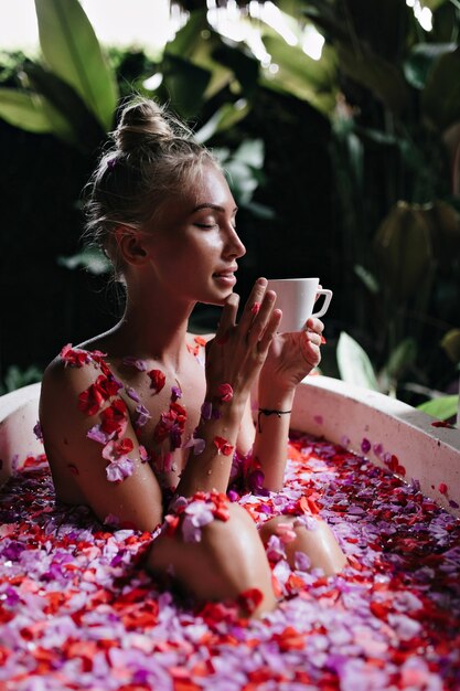 kobieta z modną fryzurę pozowanie w łazience przy filiżance herbaty. Urocza europejska dama korzystająca w weekend ze spa i pijąca kawę.
