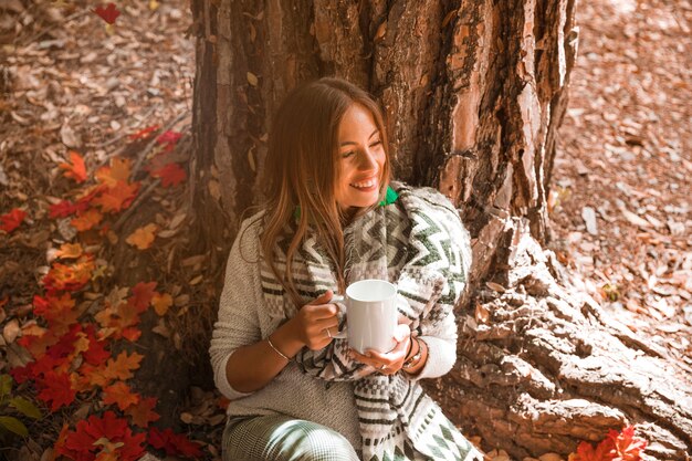 Kobieta z napojem cieszy się pogodę w jesień lesie