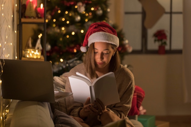 Kobieta z santa hat czytania książki przed laptopem