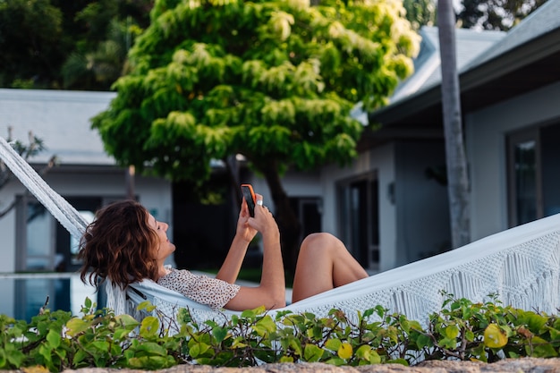 Bezpłatne zdjęcie kobieta z telefonem odpoczywa leżąc na hamaku z telefonem komórkowym