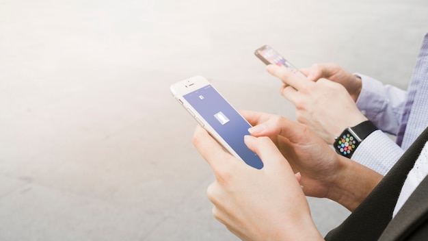 Kobieta za pomocą aplikacji facebook na telefon komórkowy w pobliżu człowieka na sobie elegancki zegarek