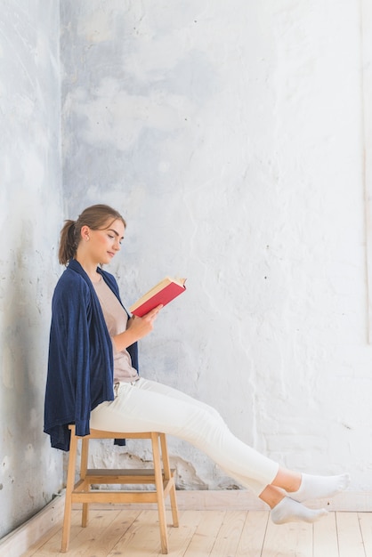 Bezpłatne zdjęcie kobiety czytelnicza książka podczas gdy siedzący na stolec w domu