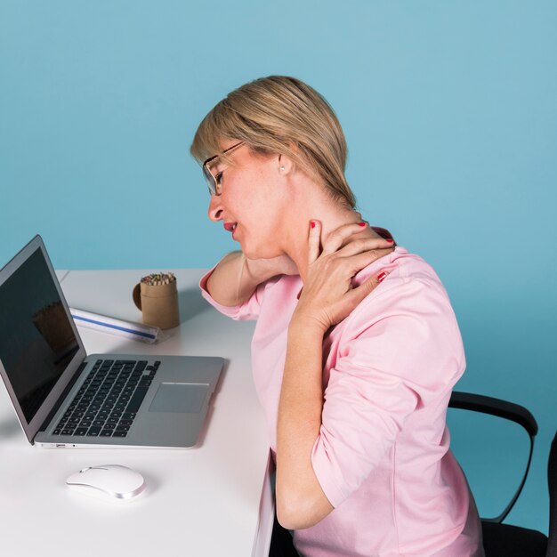 Kobiety obsiadanie w krzesło cierpieniu od szyja bólu podczas gdy używać na laptopie