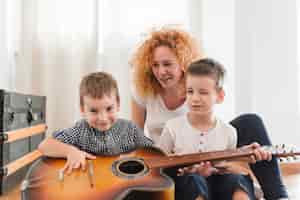 Bezpłatne zdjęcie kobiety obsiadanie z jej dziećmi bawić się gitarę