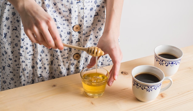 Kobiety ręka kapie miód w szkle z filiżanką herbaciane filiżanki na drewnianym biurku