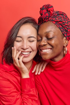 Kobiety uśmiechają się radośnie zębami cieszą się miłym dniem stoją blisko siebie śmieją się pozytywnie izolowane na żywej czerwieni