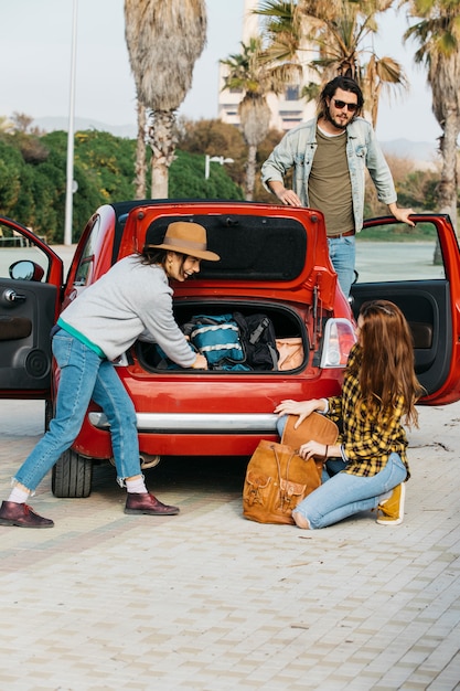 Kobiety z plecakiem w pobliżu bagażnika samochodu i człowiek wychyla się z samochodu