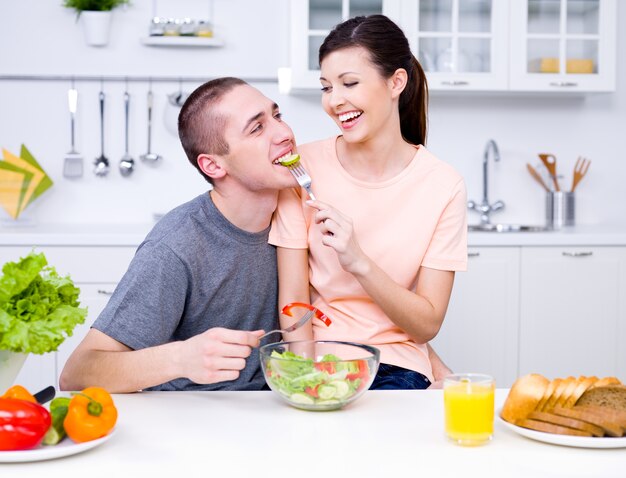 Kochająca szczęśliwa para jedzenie sałatki w kuchni - w pomieszczeniu