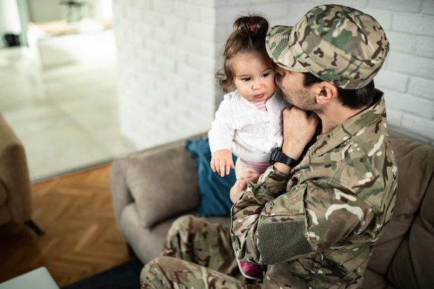 Kochający żołnierz całujący swoją małą córeczkę podczas spędzania z nią czasu w domu