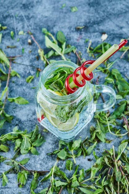 Koktajl Mojito z plasterkami limonki i mięty na niebieskim stole z listkami świeżej mięty