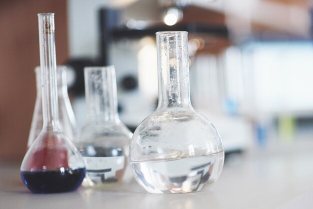Kolba z niebiesko-fioletowym różowym płynnym korkiem laboratoryjnym stoi na stole w laboratorium testowym do badania płynu.
