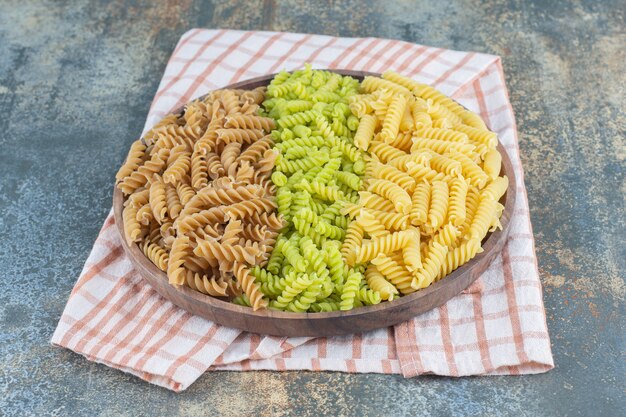 Kolorowe makarony fusilli w misce na ręcznik, na tle marmuru.