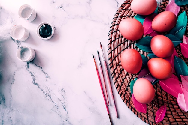 Kolorowe tło wiosna wielkanoc z kolorowymi różowymi jajkami, białymi piórami, barwnikami, pędzlami na jasnym marmurowym stole. skopiuj miejsce, widok z góry. koncepcja wesołych świąt.