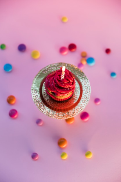 Bezpłatne zdjęcie kolorowi cukierki rozprzestrzeniający nad lekką babeczką na różowym tle