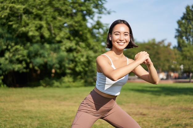 Kompleks dobrego samopoczucia i sportu, młoda azjatycka kobieta rozciągająca się, robiąca przysiady i ćwicząca na smili świeżym powietrzu