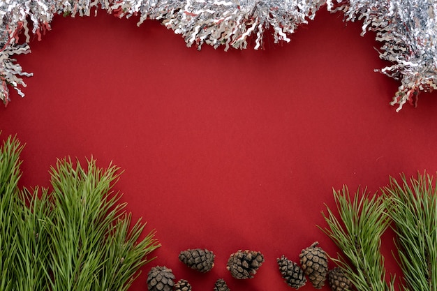 Kompozycja świąteczna. świerkowe gałęzie i shishki z białym blichtrem na czerwonym tle. płaski układanie, widok z góry, miejsce na tekst