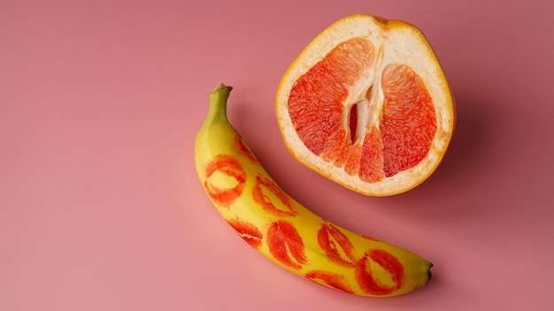 Kompozycja ze świeżego banana ze śladami czerwonej szminki i grejpfruta na różowym tle. koncepcja seksu