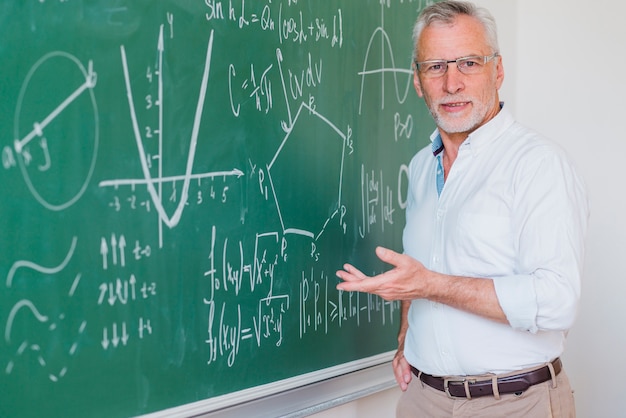 Bezpłatne zdjęcie komunikatywny męski wykładowca stoi przy blackboard i wskazuje przy równaniem