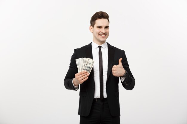 Koncepcja biznesowa - udany biznesmen posiadający banknoty dolarowe i pokazujący kciuk w górę na białym tle nad białym tłem.