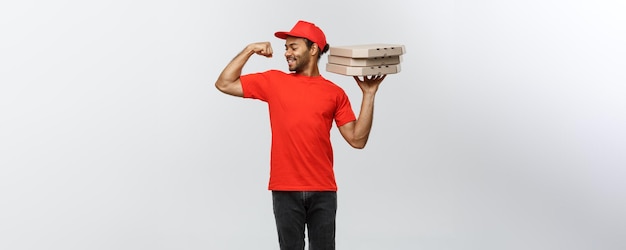 Koncepcja dostawy portret silnego afroamerykańskiego człowieka dostawy pokazującego jego mięśnie z pakietami pudełek po pizzy na białym tle na szarym tle studio Kopia miejsca