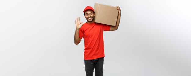 Koncepcja dostawy portret szczęśliwy afroamerykanin dostawy człowieka trzymającego pakiet pudełkowy i pokazujący znak ok izolowany na szarym tle studio kopii miejsca