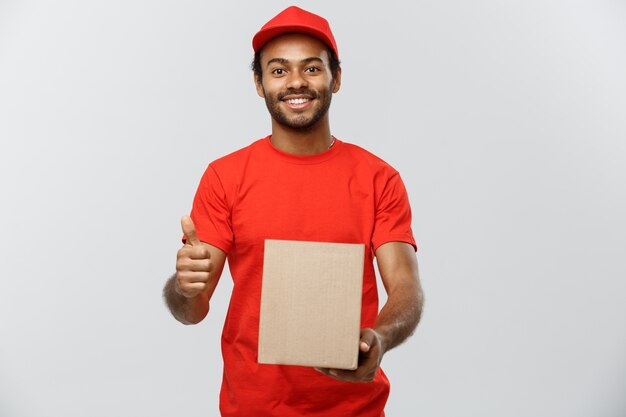 Koncepcja dostawy - Portret szczęśliwy mężczyzna Afroamerykanów dostawy pakietu pudełko i wykazujące thumps się. Pojedynczo na tle Szarym Studio. Skopiuj miejsce.