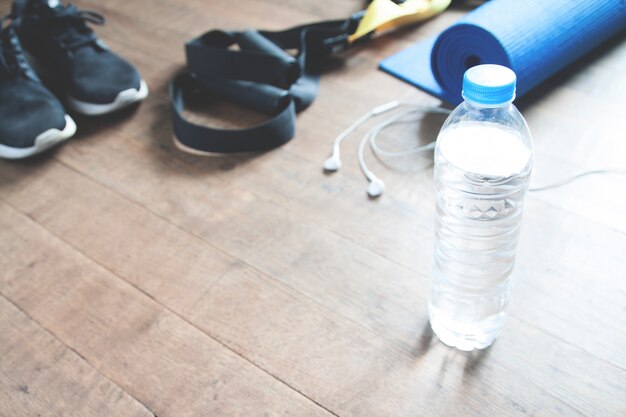 Koncepcja fitness z butelką wody, trampki, TRX, mata jogi i słuchawki na podłodze drewnianej, miejsca kopiowania