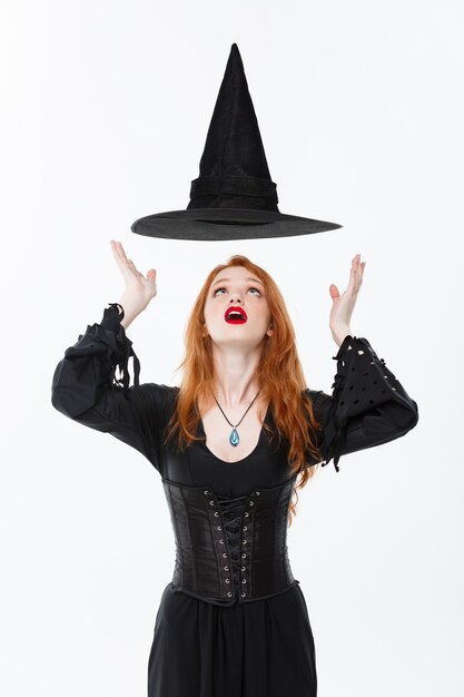 Koncepcja Halloween czarownica - Happy Halloween Sexy imbir włosy Czarownica z magicznym kapeluszu lataj?ce nad g?ow?. Na białym tle na białej ścianie.