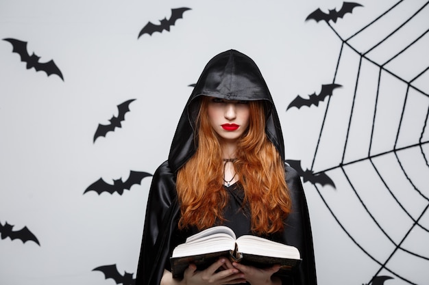Koncepcja Halloween - Piękny Ciemny Ksiądz Rzucający Zaklęcie Z Magiczną Książką Na Szarej ścianie. Darmowe Zdjęcia