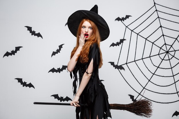 Koncepcja Halloween szczęśliwa elegancka wiedźma lubi bawić się miotłą imprezą halloweenową nad szarą ścianą