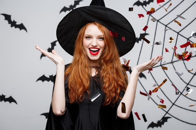 Koncepcja Halloween Witch - Szczęśliwa elegancka wiedźma rzucająca konfetti na przyjęcie z okazji halloween nad ścianą nietoperza i pająka.