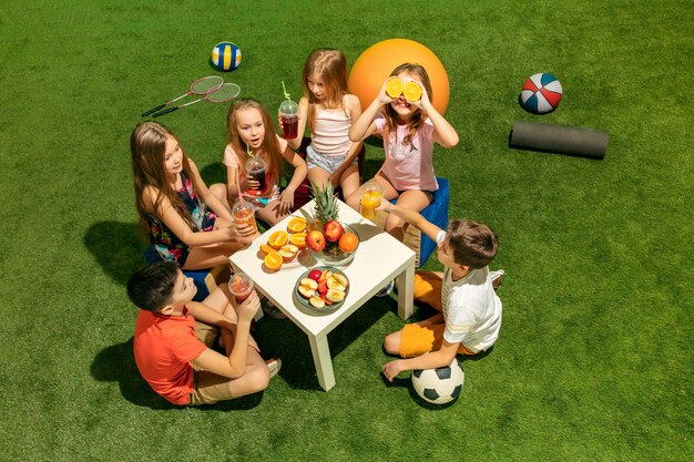 Koncepcja moda dla dzieci. Grupa nastolatków chłopców i dziewcząt siedzących na zielonej trawie w parku. Dzieci kolorowe ubrania, styl życia, koncepcje modnych kolorów.